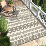 Un élégant tapis gris et blanc décoré de motifs géométriques, posé sur un parquet clair. Sur le côté, on peut voir des plantes vertes et un fauteuil à bascule en bois, créant une ambiance chaleureuse et naturelle.