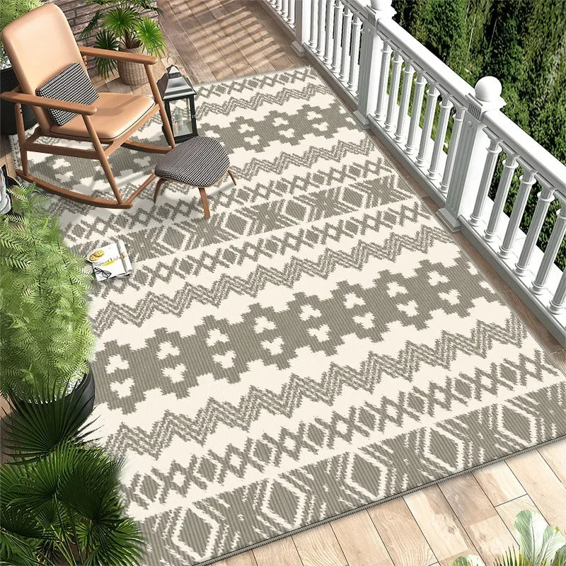 Un élégant tapis gris et blanc décoré de motifs géométriques, posé sur un parquet clair. Sur le côté, on peut voir des plantes vertes et un fauteuil à bascule en bois, créant une ambiance chaleureuse et naturelle.