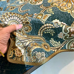 Cette image montre un motif textile décoratif fait de broderie et de motifs ornementaux dans des tons de bleu et d'or, créant un riche et élégant design.