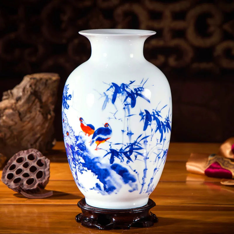 Un vase en porcelaine blanche orné de motifs bleus et rouges représentant des oiseaux et des plantes sur un fond sombre, posé sur un socle en bois.