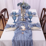 Cette table de salle à manger est élégamment décorée avec un bouquet de roses bleu-gris, des verres assortis, une nappe texturée et d'autres accessoires décoratifs, créant une atmosphère chic et raffinée.