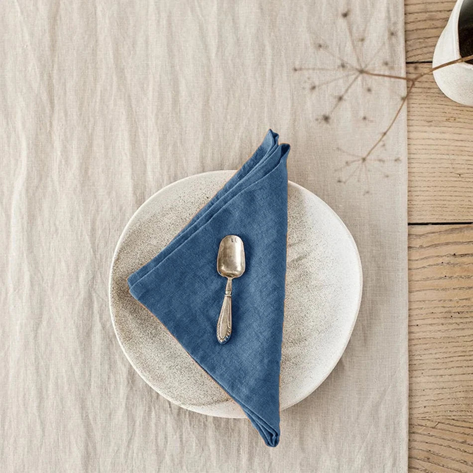 Assiette blanche et serviette en tissu bleu foncé avec une cuillère en métal sur une surface en bois.