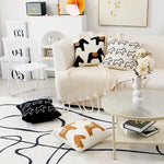 Cette image montre un salon cosy avec des coussins et décorations aux motifs graphiques blancs et noirs, donnant une ambiance épurée et design.