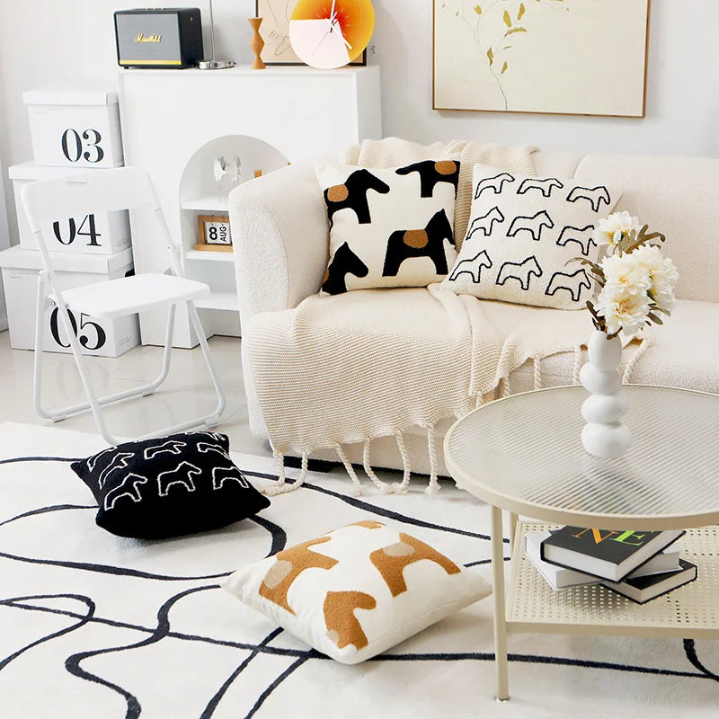 Cette image montre un salon cosy avec des coussins et décorations aux motifs graphiques blancs et noirs, donnant une ambiance épurée et design.