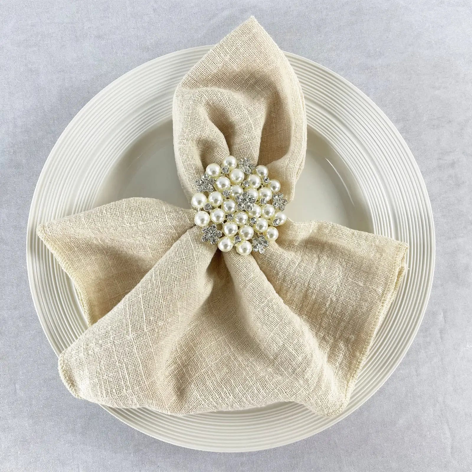 Une élégante serviette de table beige avec une broche ornée de perles et de cristaux brillants.