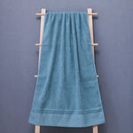 Une serviette de bain bleue suspendue sur un portant en bois contre un mur gris.