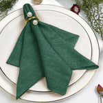 Un magnifique pli de serviette en tissu vert foncé, orné de perles blanches et entouré de fleurs décoratives sur un plateau blanc.