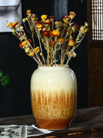 Bouquet de fleurs d'automne séchées dans un vase en céramique décoré d'un fini crème et doré, entouré de vieilles photos sur un fond sombre.