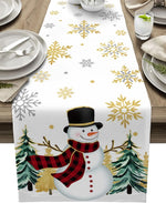 Un chemin de table blanc avec des motifs de flocons de neige dorés et argentés, ainsi qu'un bonhomme de neige vêtu d'un manteau à carreaux rouges et noir au centre, entouré de sapins stylisés.