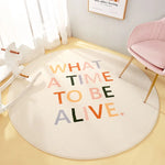 Décor de chambre avec un tapis rond et un texte "WHAT A TIME TO BE ALIVE" dans des couleurs vives sur un fond blanc.