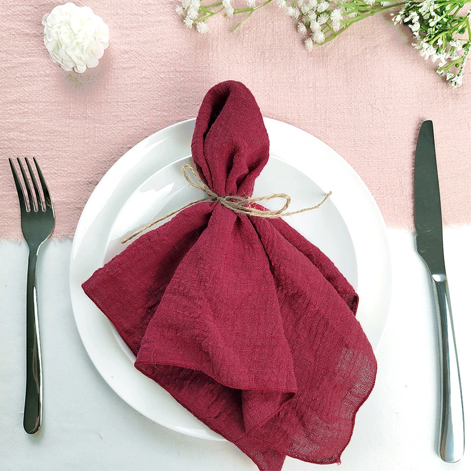 Serviette en lin de couleur bordeaux enroulée et attachée avec une ficelle, sur une assiette blanche, entourée de fleurs blanches