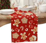 Une table de fête décorée pour Noël avec de la vaisselle blanche, des verres de cristal et un chemin de table rouge orné de motifs de bonhommes en pain d'épice et de flocons de neige.