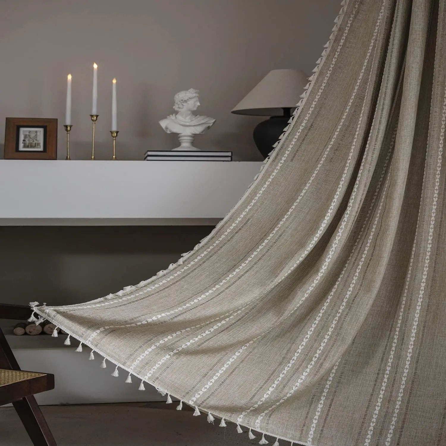 Voilage rayé beige à pompons décoratifs suspendu dans un salon au style bohème chic avec bougies et décoration classique.