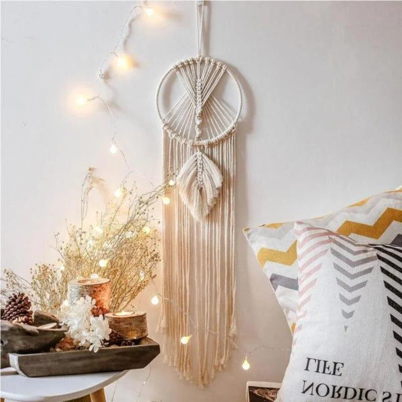 Attrape-rêves bohème décoratif suspendu au mur avec guirlandes lumineuses, accompagné de coussins colorés et d'éléments naturels, créant une ambiance chaleureuse et apaisante pour un intérieur tendance.