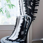 Élégante écharpe noire et blanche à motifs de violons, drapée sur une chaise design près d'une fenêtre lumineuse, ajoutant une touche musicale raffinée à votre intérieur. Accessoire parfait pour les amateurs de musique et de mode, idéal pour sublimer votre style en toute saison.