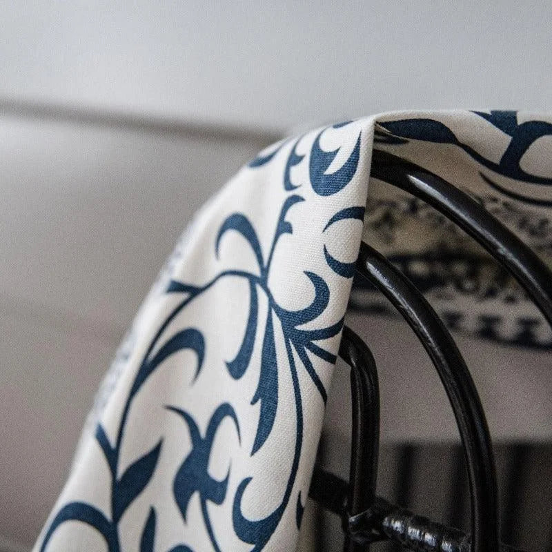 Serviette élégante avec motifs floraux bleus, drapée sur une chaise en métal noir, ajoutant une touche sophistiquée à la décoration intérieure.