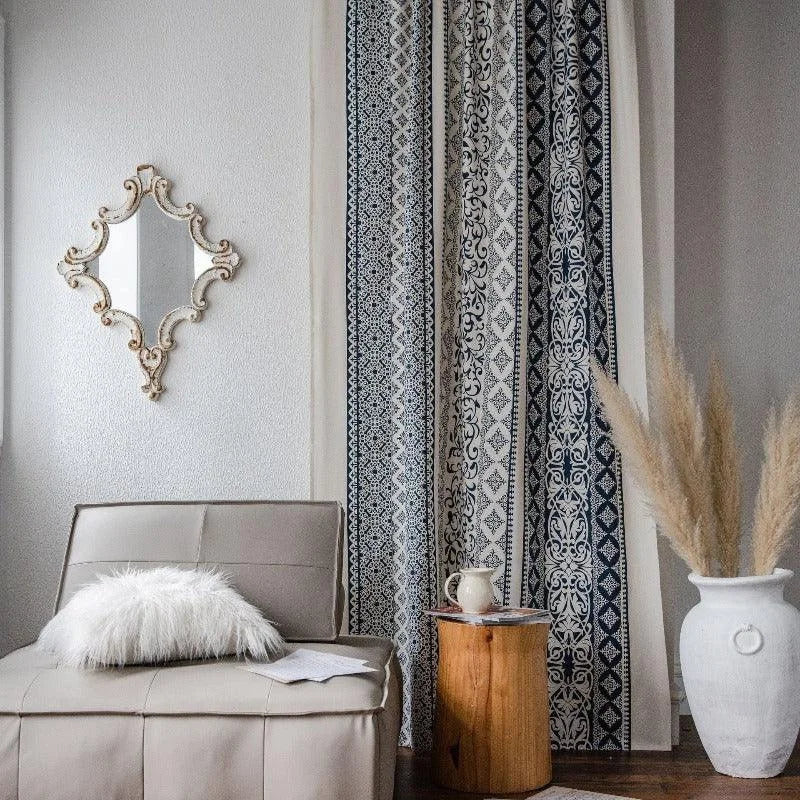 Salon élégant avec canapé moderne et coussin décoratif, rideau à motifs géométriques noirs et blancs, table d'appoint en bois, miroir mural orné, et vase blanc avec pampas. Ambiance chaleureuse et intemporelle pour un intérieur raffiné.