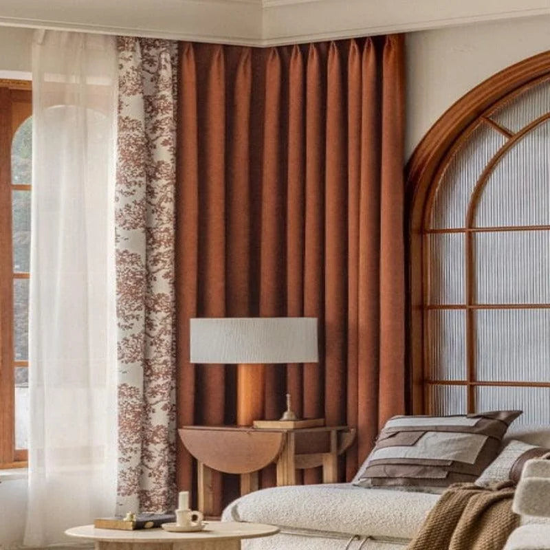 Rideaux élégants pour salon moderne, offrant une combinaison de couleurs chaudes et motifs subtils. Fenêtre cintrée ajoutant une touche classique, avec un canapé confortable et une lampe design sur une table d'appoint. Parfait pour une décoration intérieure raffinée et accueillante.