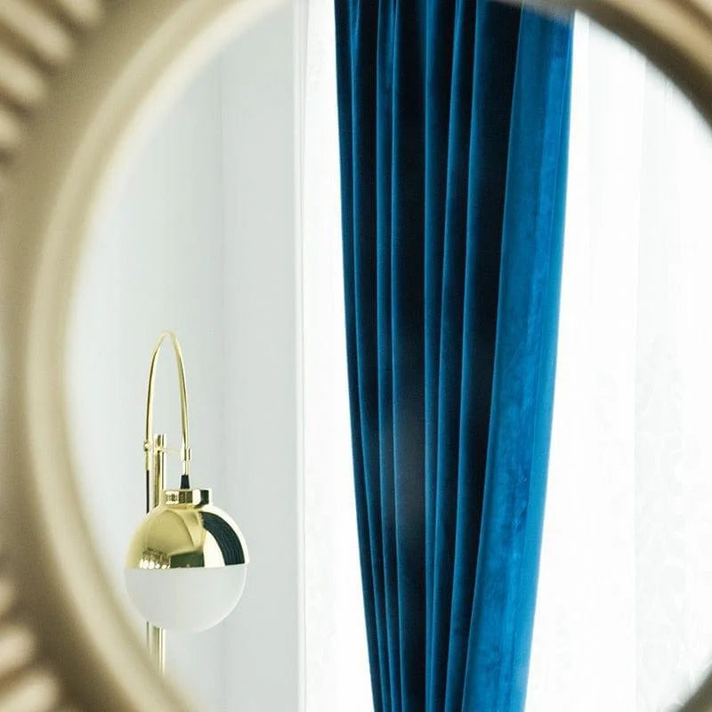 Miroir design doré reflétant une lampe élégante et un rideau bleu dans un intérieur moderne. Décoration d'intérieur sophistiquée avec des éléments de style et de confort.