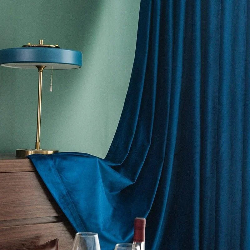 Lampe de table élégante avec abat-jour bleu, posée sur une table en bois, avec des rideaux bleus offrant un style sophistiqué. Atmosphère moderne et design, idéale pour un salon ou une chambre tendance.