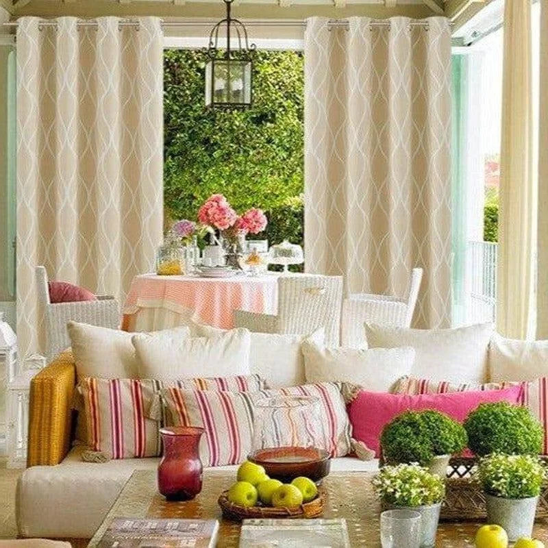 Salle de séjour lumineuse avec rideaux élégants, décorée de coussins colorés et d'une table ornée de fleurs roses. Ambiance de détente avec vue sur un jardin verdoyant, idéale pour se relaxer en famille. Parfait pour un espace de vie accueillant et chaleureux.