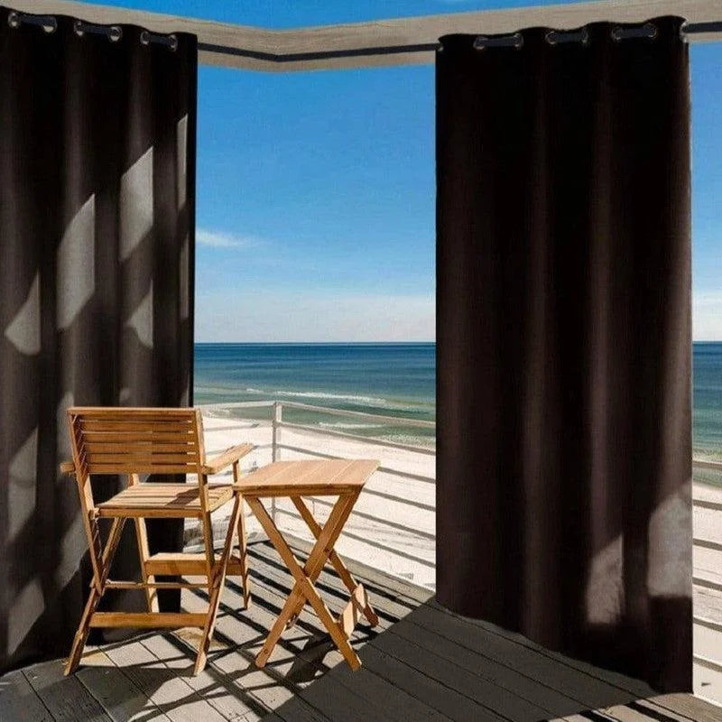 Rideau d'extérieur occultant noir pour terrasse avec vue sur mer. Idéal pour créer un espace privé tout en profitant de l'environnement extérieur, parfait pour ombrager votre balcon ou patio. Mobilier en bois et vue panoramique sur l'océan.