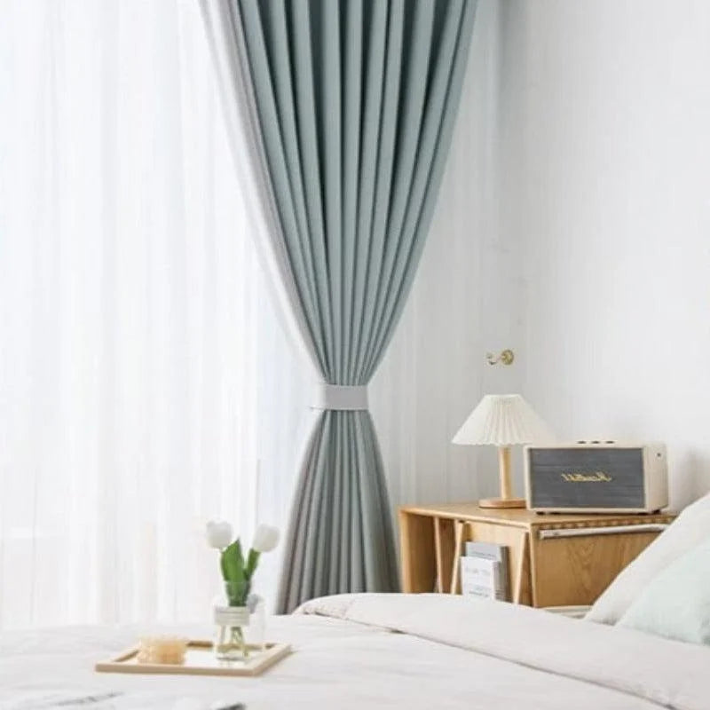 Chambre lumineuse avec rideaux obscurcissants gris élégants, offrant une décoration moderne et apaisante. Vue sur un lit confortable et une table de chevet avec une lampe design, parfait pour créer une ambiance cocooning et relaxante dans la chambre à coucher.