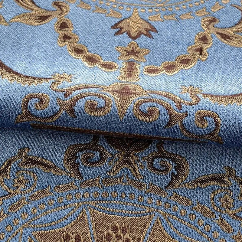Image d'un tissu bleu avec un motif brodé doré et brun, idéal pour la décoration intérieure, apportant une touche d'élégance et de raffinement à votre espace de vie. Design complexe et ornemental, parfait pour des projets de couture ou d'ameublement sur mesure.