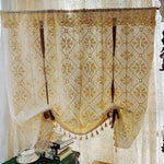 Rideau ajouré beige avec motif floral suspendu devant une fenêtre. Il décore élégamment un espace lumineux, appendi au-dessus de livres et d'une tasse de thé, créant une ambiance chaleureuse et accueillante. Parfait pour ajouter une touche romantique et rustique à tout intérieur.
