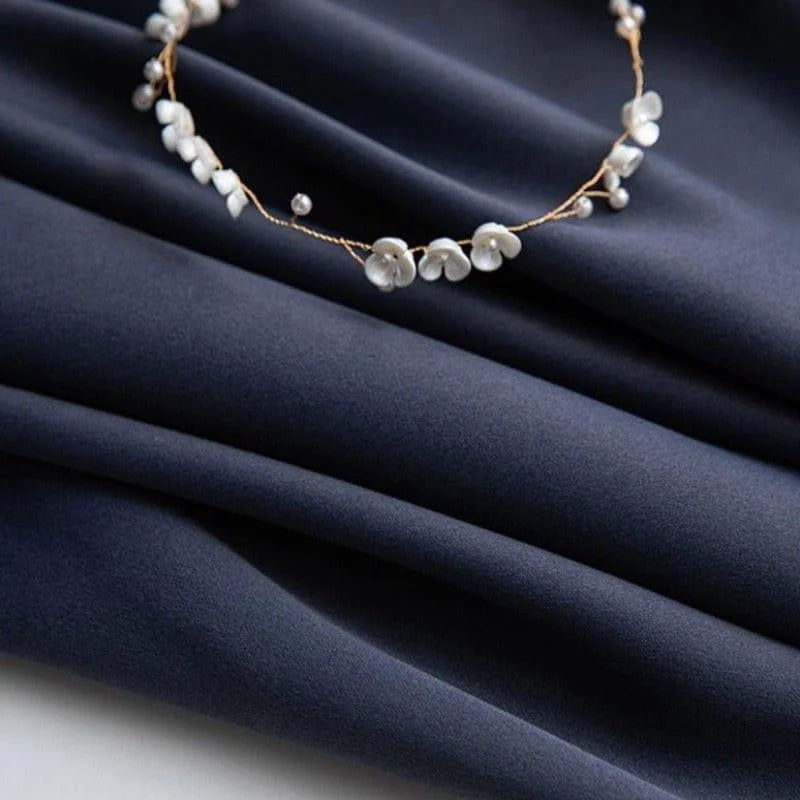 Image d'un tissu bleu foncé, délicatement orné d'un élégant bracelet de petites fleurs blanches, parfait pour créer une ambiance raffinée et sophistiquée dans vos créations textiles ou vos aménagements d'intérieur.