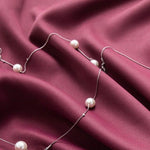 Collier élégant avec perles posé délicatement sur un tissu violet foncé. Accessoire de mode sophistiqué idéal pour compléter une tenue chic et raffinée. Parfait pour des occasions spéciales ou des soirées habillées.