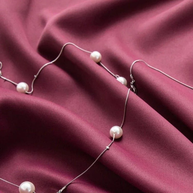 Collier élégant avec perles posé délicatement sur un tissu violet foncé. Accessoire de mode sophistiqué idéal pour compléter une tenue chic et raffinée. Parfait pour des occasions spéciales ou des soirées habillées.