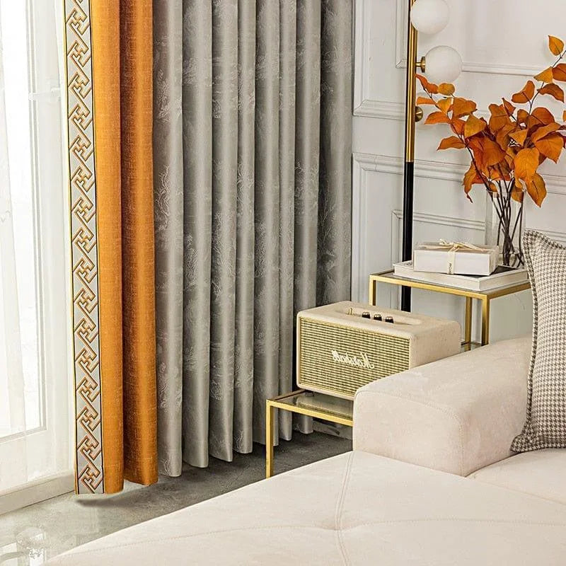 Rideaux modernes gris et orange avec motifs géométriques, ajout élégant à un salon contemporain. Accents dorés sur les tables, vase avec feuilles colorées, offrant une touche automnale. Idéal pour une décoration intérieure sophistiquée et chaleureuse.
