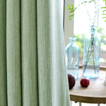 Rideau vert pastel élégant dans un intérieur lumineux avec des bouteilles décoratives en verre et des éléments naturels, parfait pour une ambiance sereine et moderne.