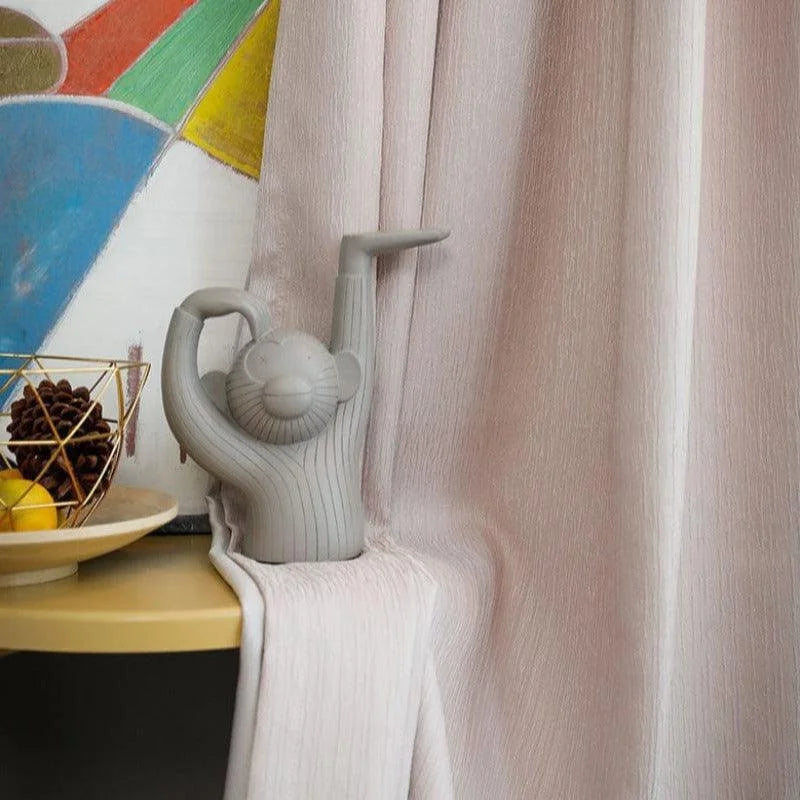 Statue décorative en forme de singe au design moderne, parfaite pour embellir votre intérieur avec une touche ludique. Placée devant un rideau rose pâle, cette pièce unique attire le regard avec son style épuré. Idéale sur une étagère ou un buffet, elle crée une ambiance chaleureuse.