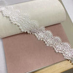 Dentelle délicate blanche ornée de perles élégantes sur un fond pastel, idéale pour la décoration intérieure et les projets de couture créatifs. Parfait pour ajouter une touche raffinée à vos créations artisanales.
