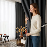 Femme souriante fermant un rideau gris anthracite occultant dans un salon moderne décoré avec des tons neutres et des touches dorées.