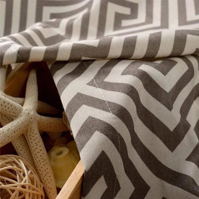 Tissu décoratif à motifs géométriques zigzag gris et blanc, idéal pour la décoration d'intérieur moderne. Parfait pour créer une ambiance élégante et sophistiquée. Accessoires marins en arrière-plan ajoutant une touche de bord de mer.
