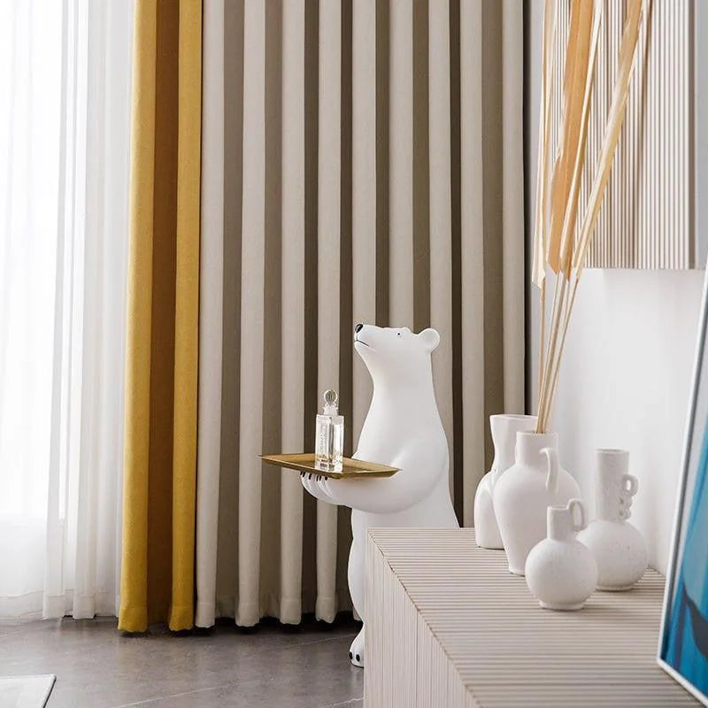 Décoration intérieure moderne avec une sculpture originale d'ours tenant un plateau, ajoutant une touche ludique à l'espace. Rideaux élégants en arrière-plan et vases décoratifs sur un meuble, créant une ambiance harmonieuse et contemporaine dans le salon. Accessoire unique pour sublimer votre intérieur.