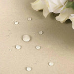 Texte alternatif : "Gouttes d'eau sur une surface beige imperméable avec des fleurs blanches en arrière-plan. Protection efficace contre l'humidité et les liquides."