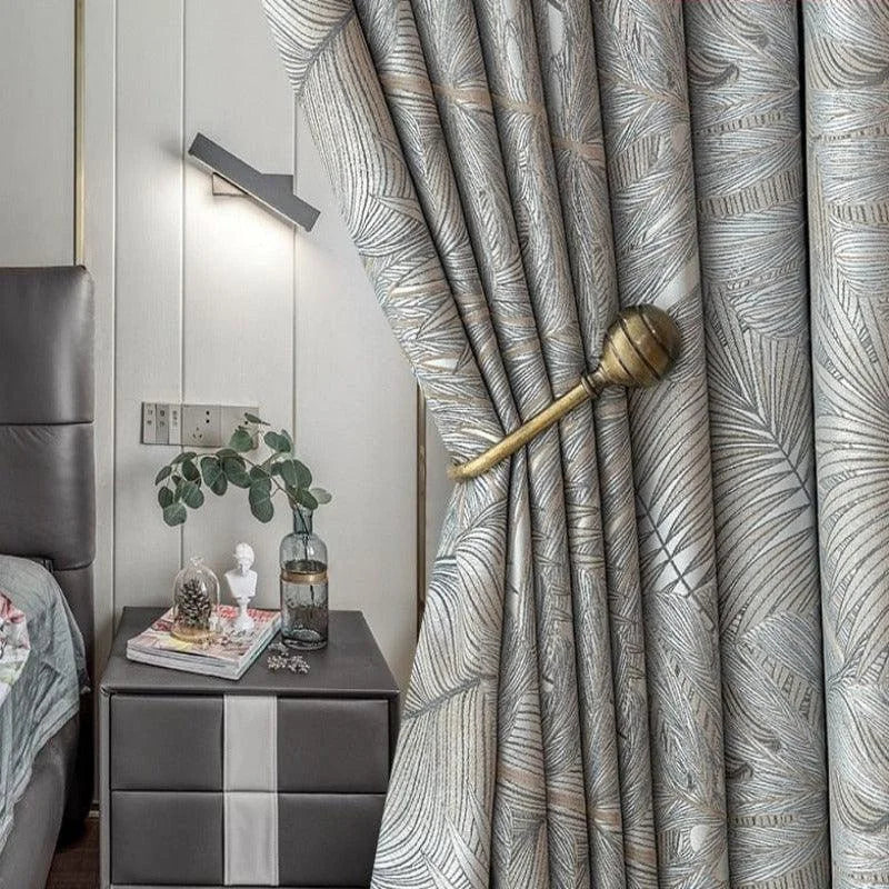 Rideaux modernes avec motif foliaire, ajoutant une touche élégante à la décoration intérieure d'une chambre contemporaine. L'agencement avec une embrasse dorée souligne le style raffiné tout en permettant de moduler la luminosité selon les envies. Parfaits pour apporter du cachet à votre espace de vie.