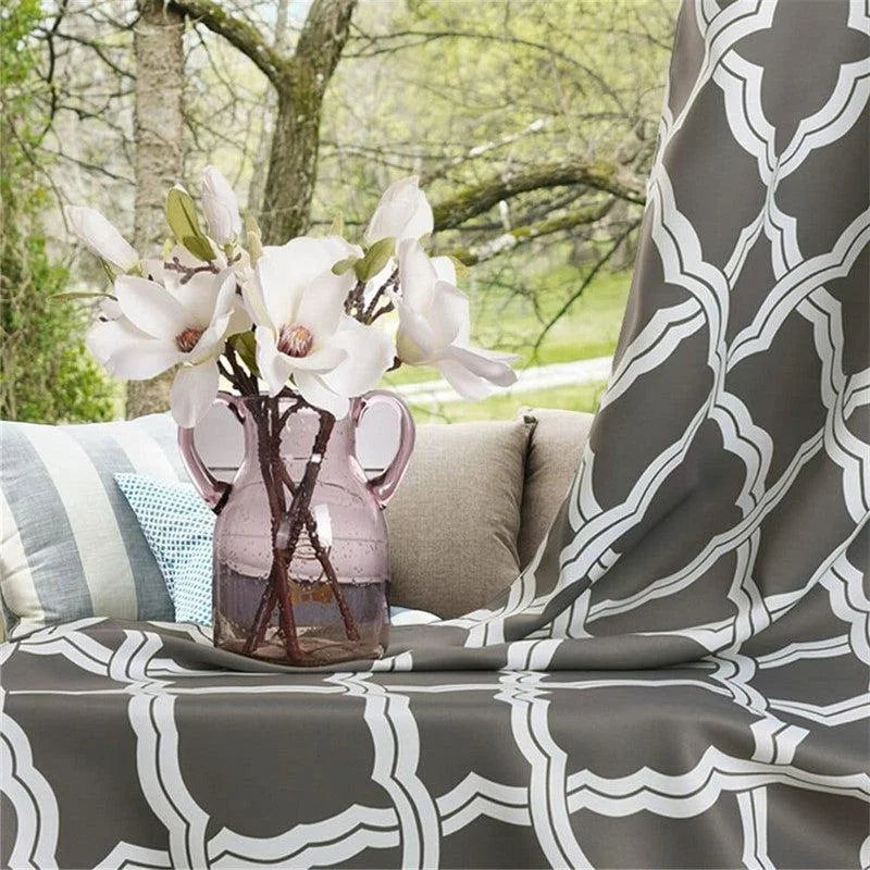 Vase décoratif rose avec fleurs blanches sur un tissu à motifs géométriques gris et blanc, idéal pour embellir votre intérieur ou terrasse. Ambiance naturelle et élégante pour votre espace de détente.