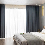 Chambre moderne avec rideaux opaques gris foncé et voilages blancs, éclairage mural design, lit double confortable, ambiance élégante et apaisante, idéal pour une décoration intérieure contemporaine.