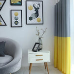 Voici une suggestion de texte alternatif :

"Salon moderne avec canapé gris, meuble d'appoint blanc à pieds en bois, rideaux bicolores gris et jaunes, et décorations murales géométriques. Vase élégant avec branches fleuries apportant une touche naturelle."