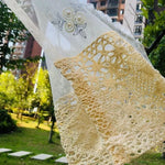 Écharpe élégante en dentelle beige avec motifs floraux, suspendue dans un jardin verdoyant, idéale pour les tenues estivales. Cette pièce unique ajoute une touche de sophistication et de raffinement à votre style, parfaite pour les occasions spéciales ou un usage quotidien. Découvrez comment cet accessoire polyvalent peut rehausser votre garde-robe avec charme et élégance.