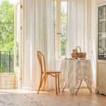 Chaise élégante et table avec nappe décorative dans une pièce lumineuse avec baies vitrées, vue sur jardin extérieur. Ambiance naturelle et détente assurée. idéal pour un coin lecture ou un petit déjeuner ensoleillé.