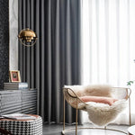 Fauteuil design moderne avec structure dorée, installé dans un salon contemporain élégant. Il est agrémenté d'un coussin orange et d'un plaid douillet, placé près de rideaux sombres et d'une lampe suspendue chic. L'ambiance chaleureuse et sophistiquée est idéale pour un intérieur raffiné.