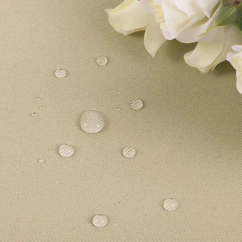 Image montrant un tissu beige avec des gouttes d'eau isolées, démontrant un effet imperméable. Des fleurs blanches apparaissent dans le coin supérieur droit, ajoutant une touche élégante. Ce produit associe fonctionnalité et esthétique pour une décoration intérieure raffinée. Idéal pour ceux cherchant à allier protection et design dans leur espace de vie.