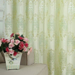 Rideau élégant à motifs baroques dorés et verts, ajoutant une touche de sophistication à la décoration intérieure. Parfait pour créer une ambiance chaleureuse dans le salon. Arrière-plan idéal pour mettre en valeur un arrangement floral de roses roses et rouges sur un canapé beige.