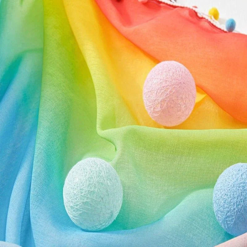 Écharpe aux couleurs de l'arc-en-ciel accompagnée de boules décoratives pastel. Accessoires décoratifs parfaits pour ajouter une touche de couleur vive à votre intérieur. Idéal pour la maison, offrant une atmosphère joyeuse et colorée.